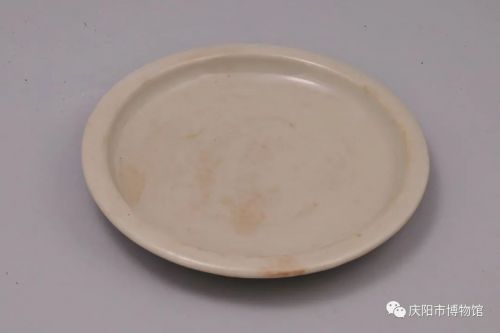 耀州窯月白釉蓮花紋瓷盤  金代，國家一級(jí)文物。華池縣五蛟公社李良子隊(duì)窖藏出土。高2.4厘米， 口徑18.9 厘米，底徑3.5了厘米。平沿，厚唇，淺腹，平底內(nèi)凹，近底處露胎。內(nèi)外施青釉，釉汁瑩潤，盤內(nèi)底印有盛開的荷花和碩大的荷葉，為耀州窯瓷器中的精品，具有很高的藝術(shù)價(jià)值。