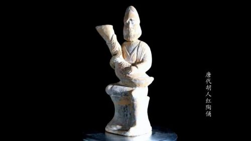 唐代胡人俑，高40厘米。胡人頭戴幞頭帽，尖鼻深目，雙睛圓睜，留八字胡，鬢及頦下有長髯。雙手抱一鴨形皮囊，身穿翻領衣，腰系帶，足穿靴，左腿下垂，右腿盤坐在一高座上。
